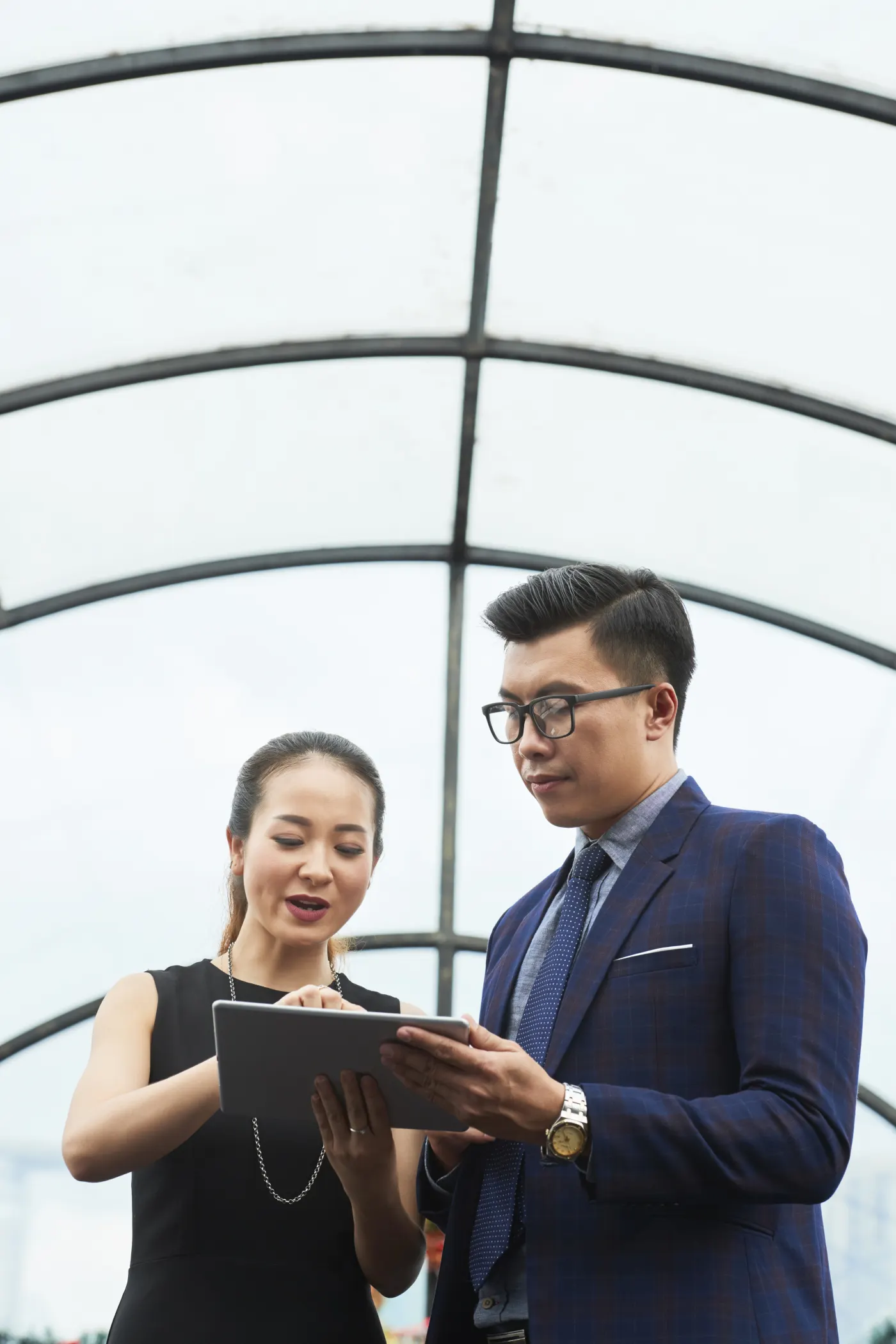 Two professionals examine figures together on a tablet under a glass roof.
