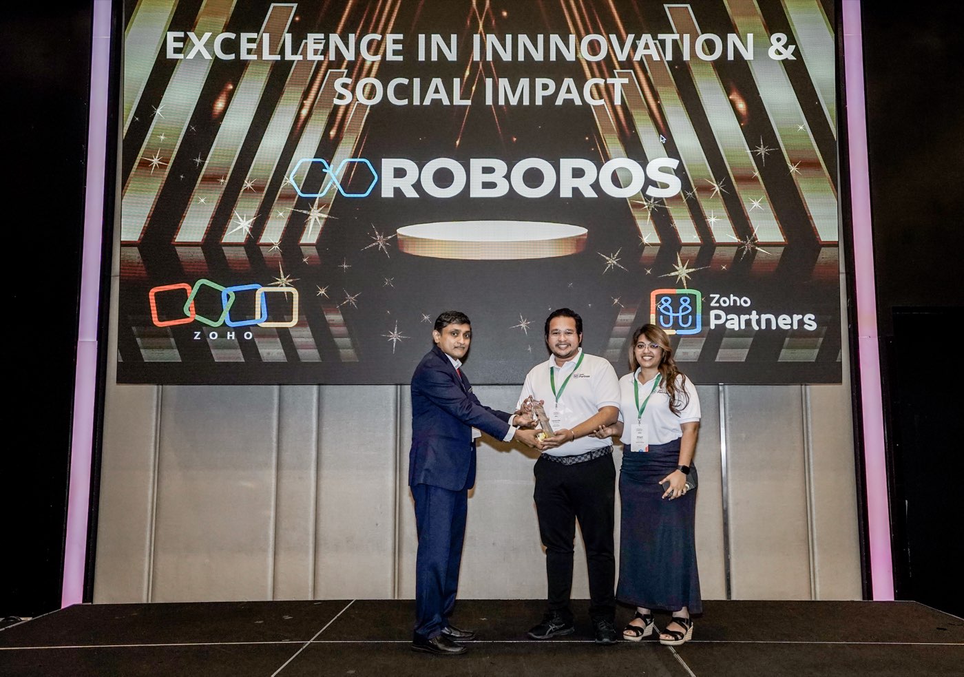 Ooroboros receiving the Zoho APAC Partner Innovation Excellence & Social Impact Award on stage — the company name on the big screen behind the team